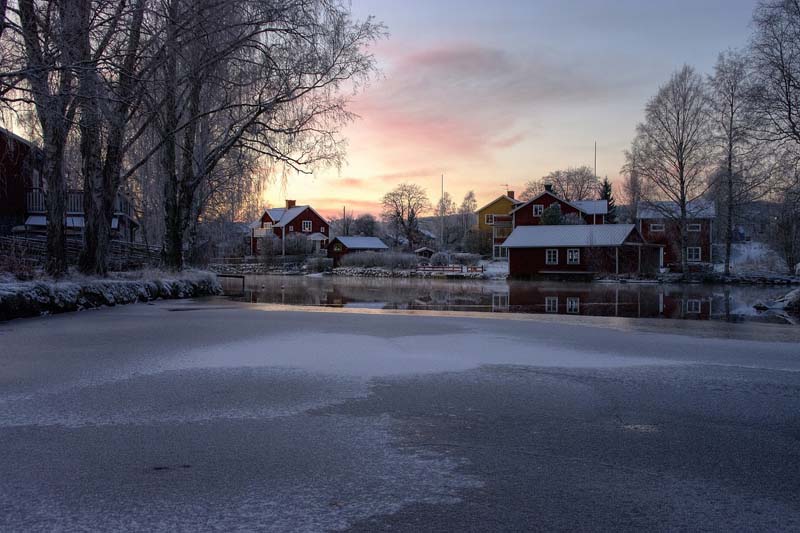 Röda trähus vid sjön i Falun med vintersolnedgång